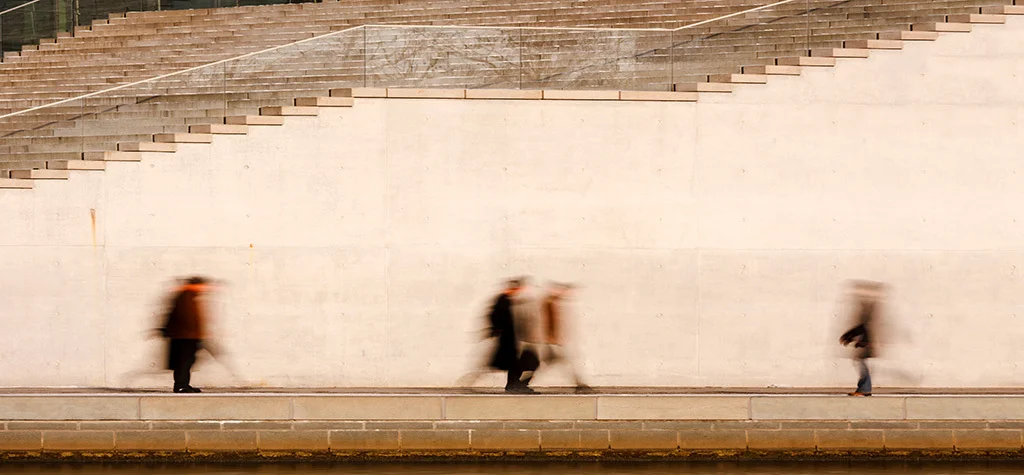 3 blurry people shadows along a high wall