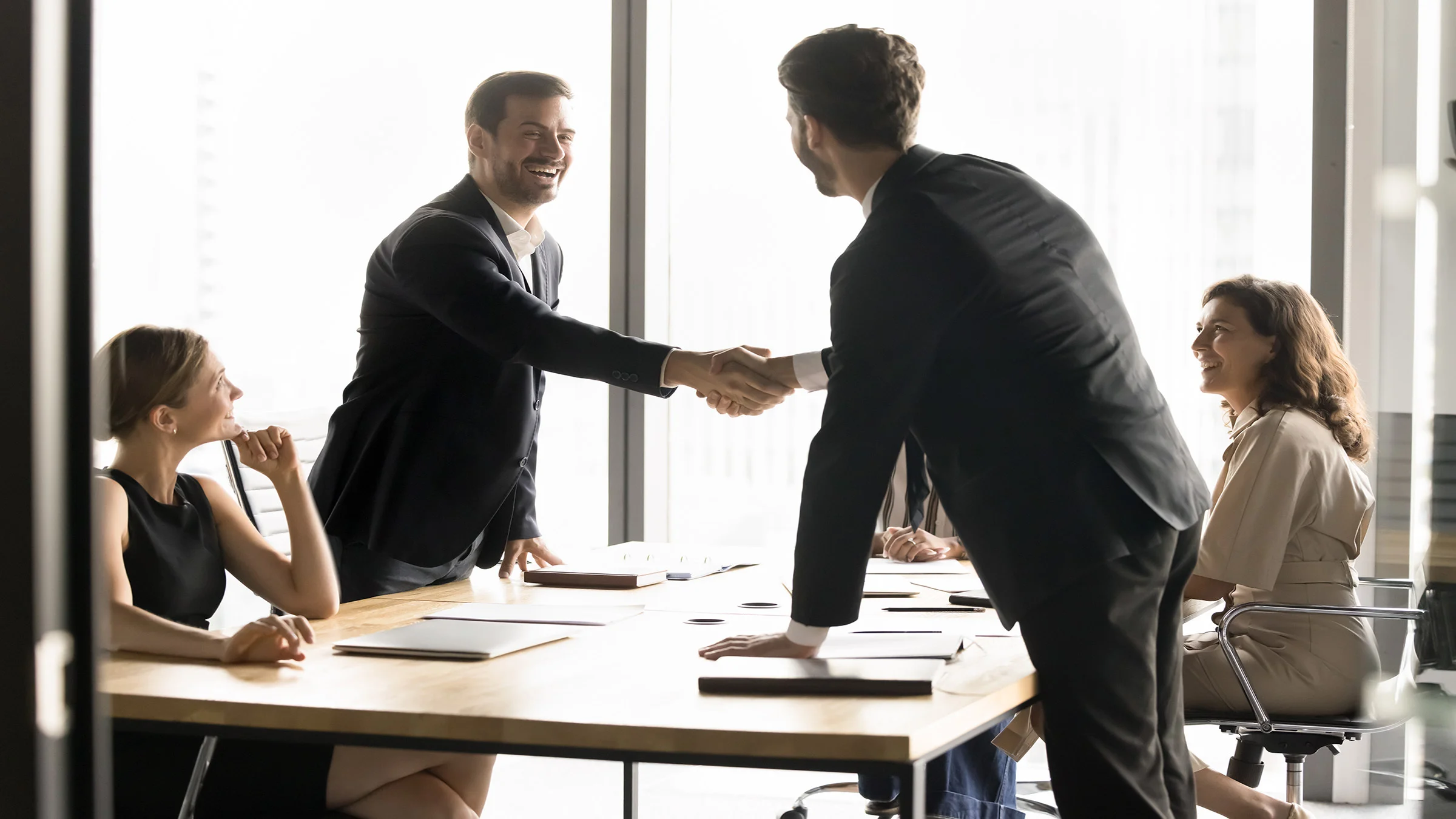 2 men shaking hands around a conference room table