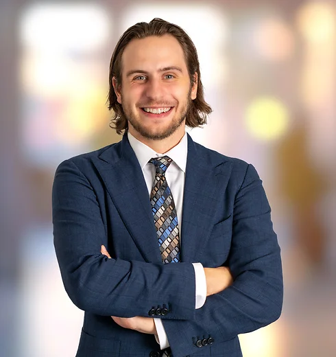 Smiling Brandan Goodwin in a dark blue suit with his arms crossed