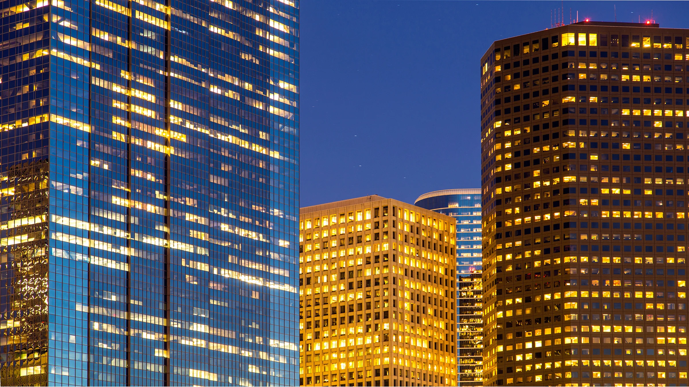 3 high rise buildings with windows lit at dusk