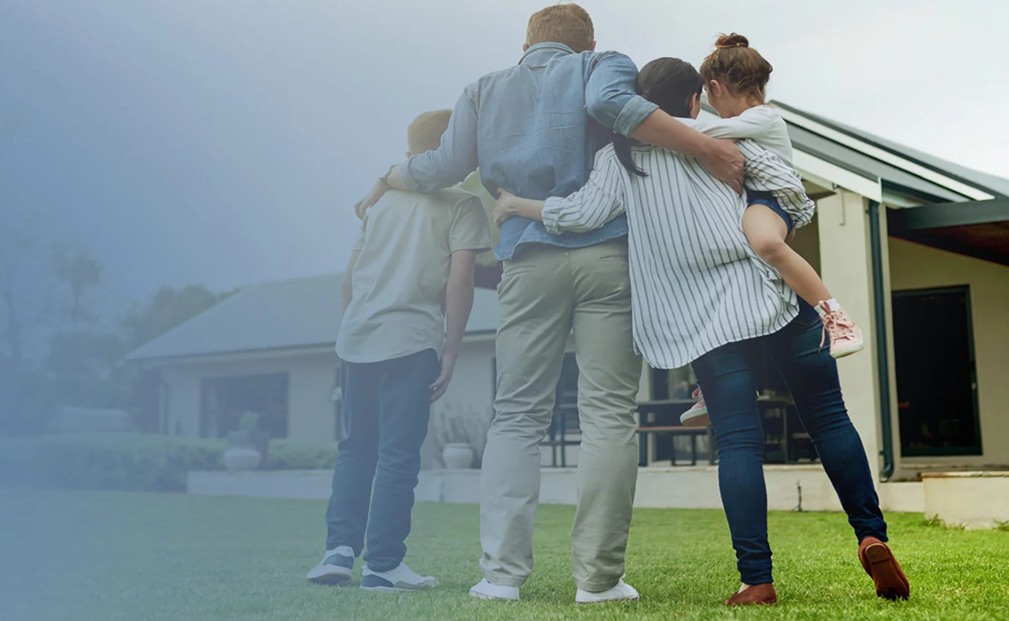 A couple and their two kids with their arms around each other in front of a house