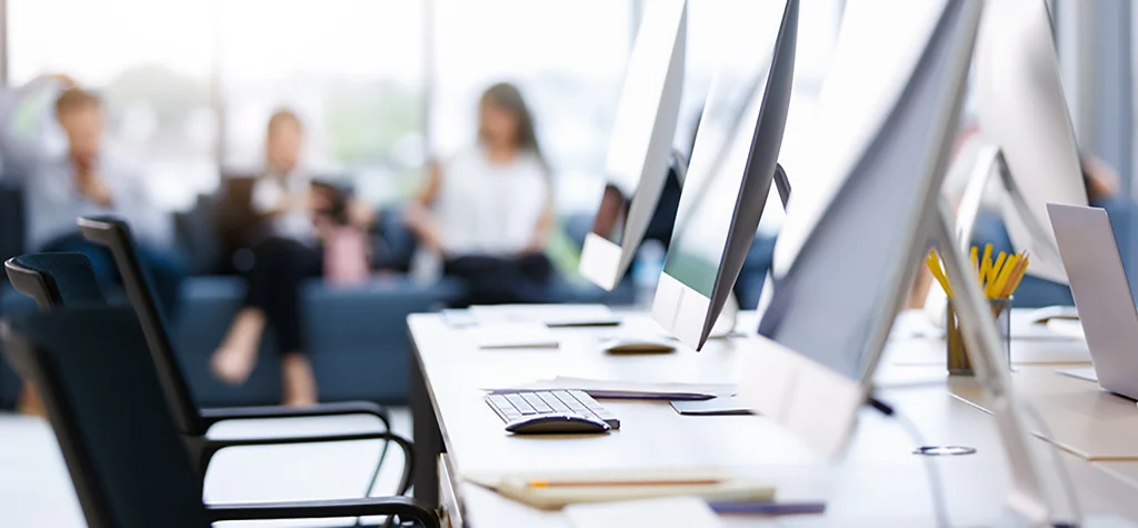 Computers in the foreground, blurry people talking on a couch in the background