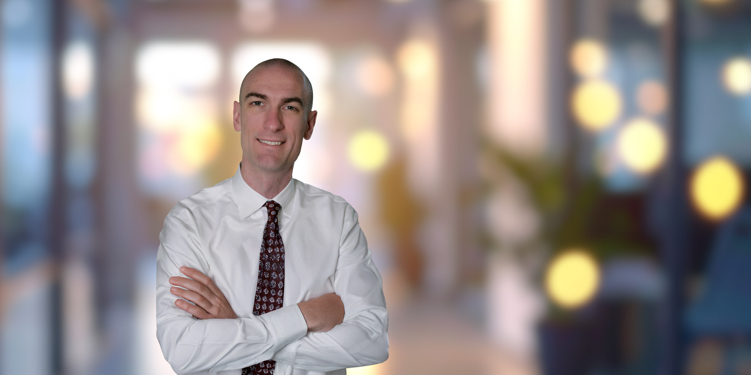 Tony Basch standing with arms crossed in white button-up and patterned tie