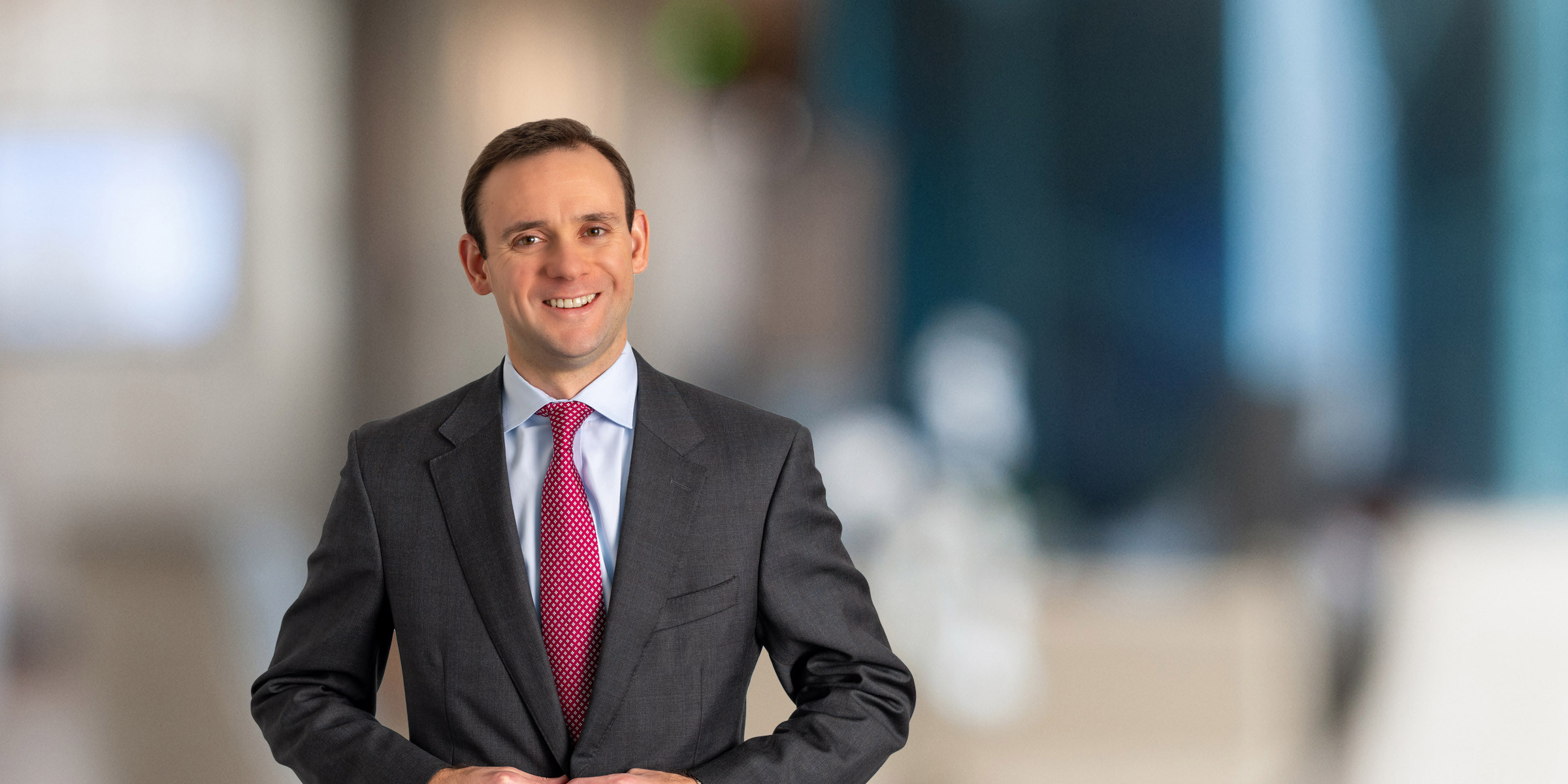 Brandon Allred in dark gray suit with red tie