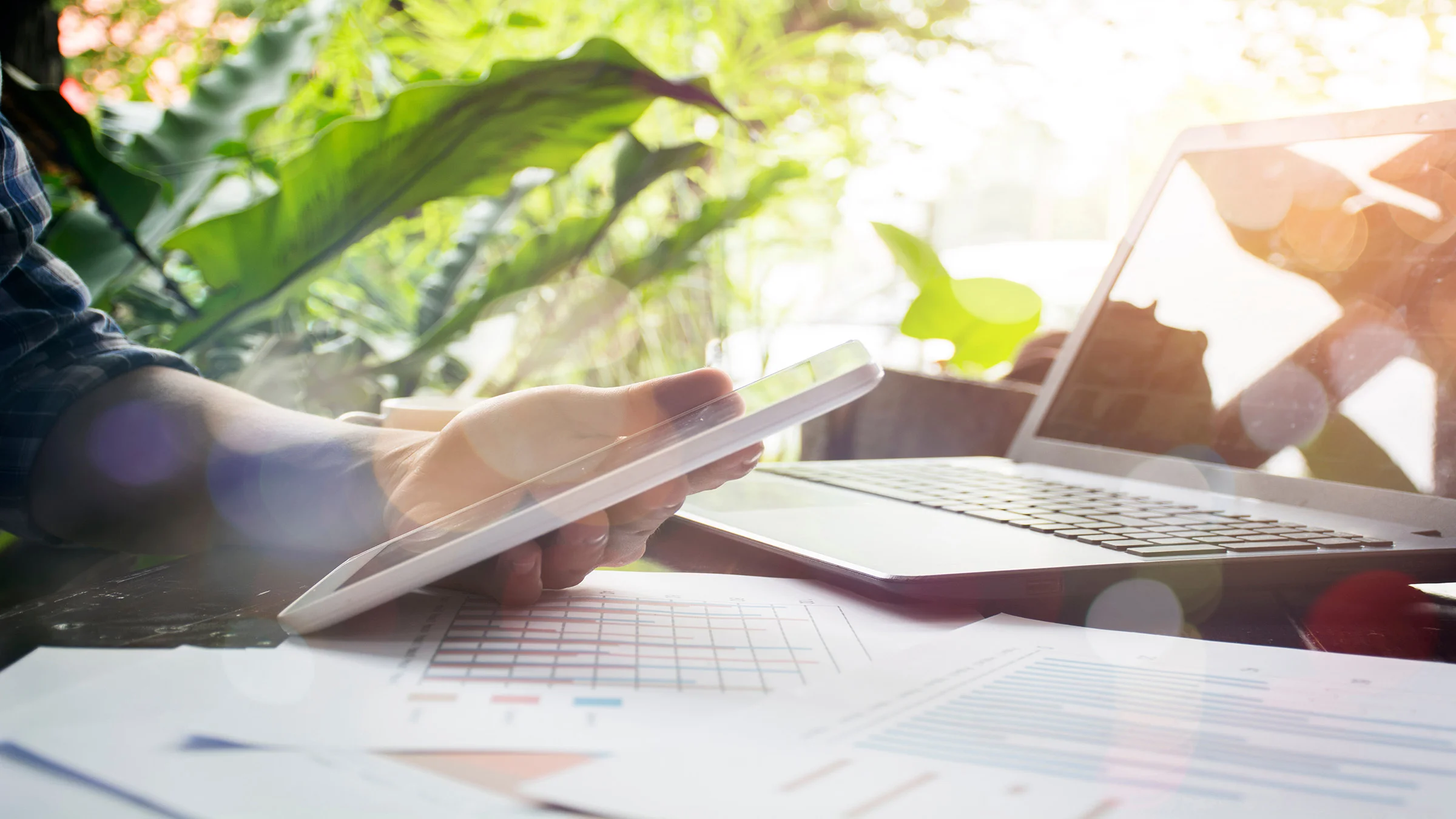 Hand holding a tablet with a laptop nearby