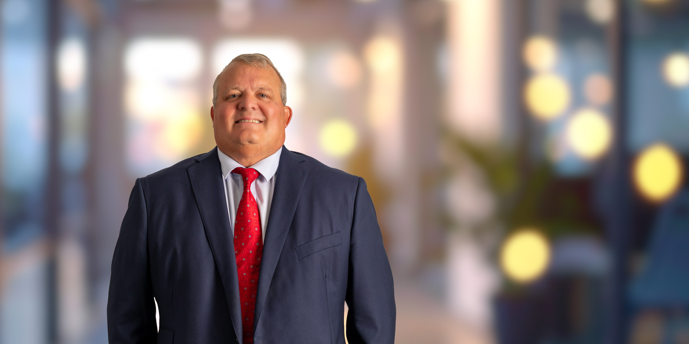 Braxton McKee smiling in a dark suit and red tie