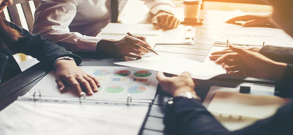 Hands around a conference table with papers in the middle