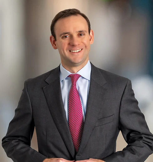 Brandon Allred in dark gray suit with red tie