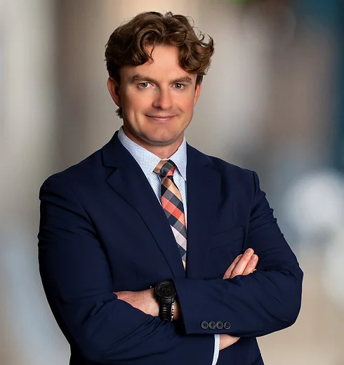 Cameron Dunnavant with his arms crossed, in a black suit and plaid tie