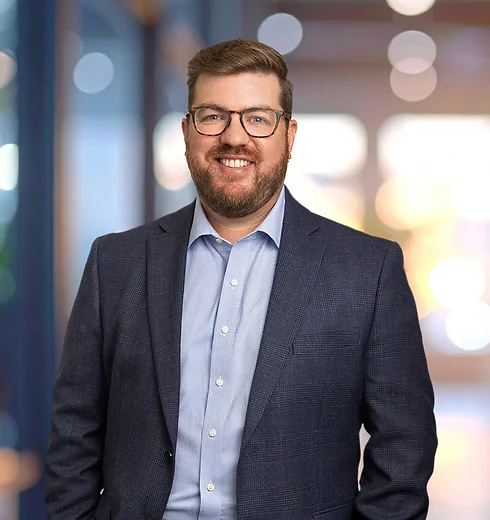 Colin McCarthy wearing a dark suit with a light blue shirt open at the collar