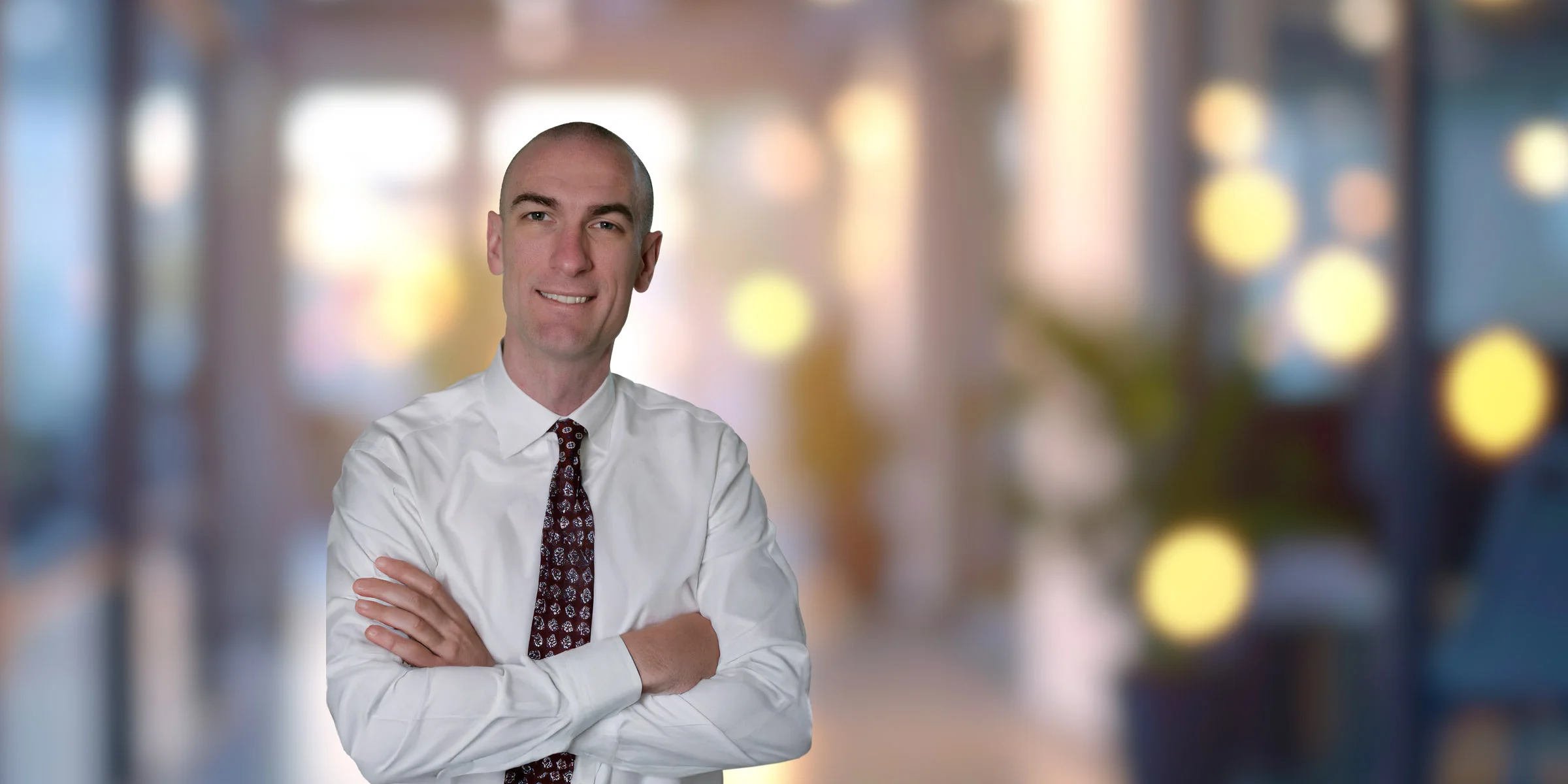 Tony Basch standing with arms crossed in white button-up and patterned tie