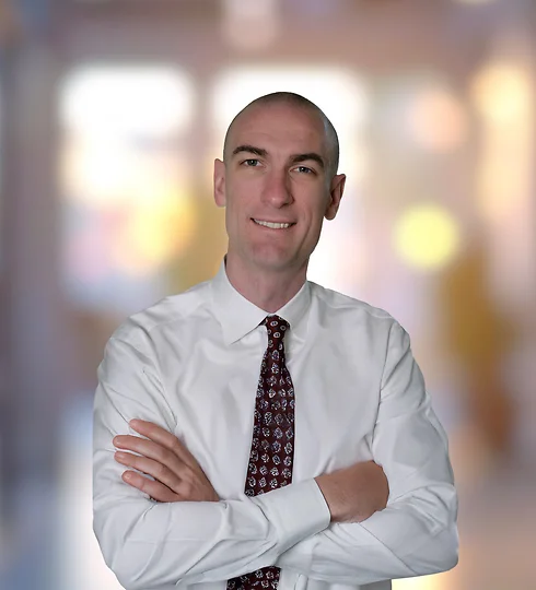 Tony Basch standing with arms crossed in white button-up and patterned tie