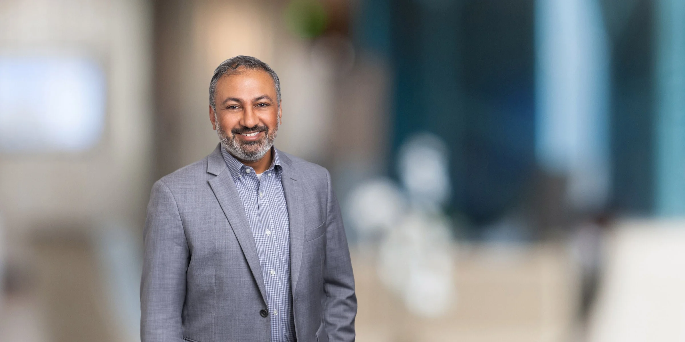 Smiling Rakesh Parikh in a silver suit with a blue checked shirt