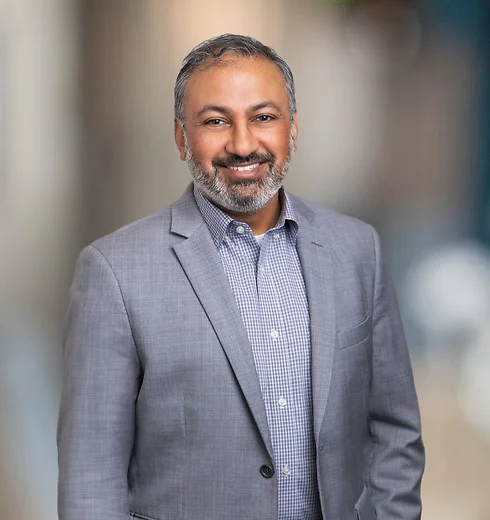 Smiling Rakesh Parikh in a silver suit with a blue checked shirt