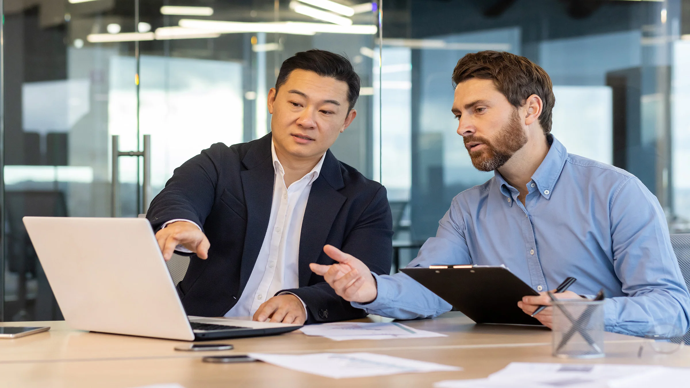 2 business men sitting at a table pointing at a computer