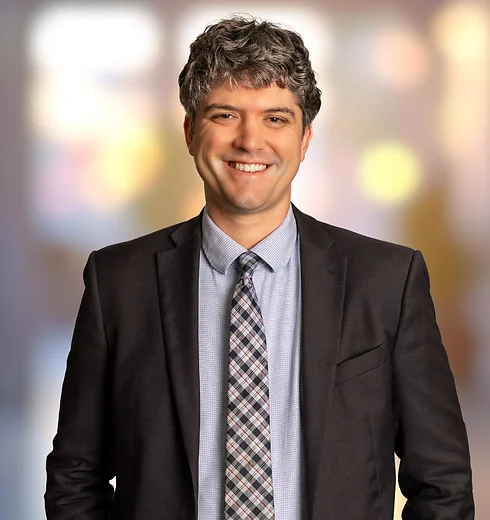Adam Pratt smiling with a dark suit and a blue shirt